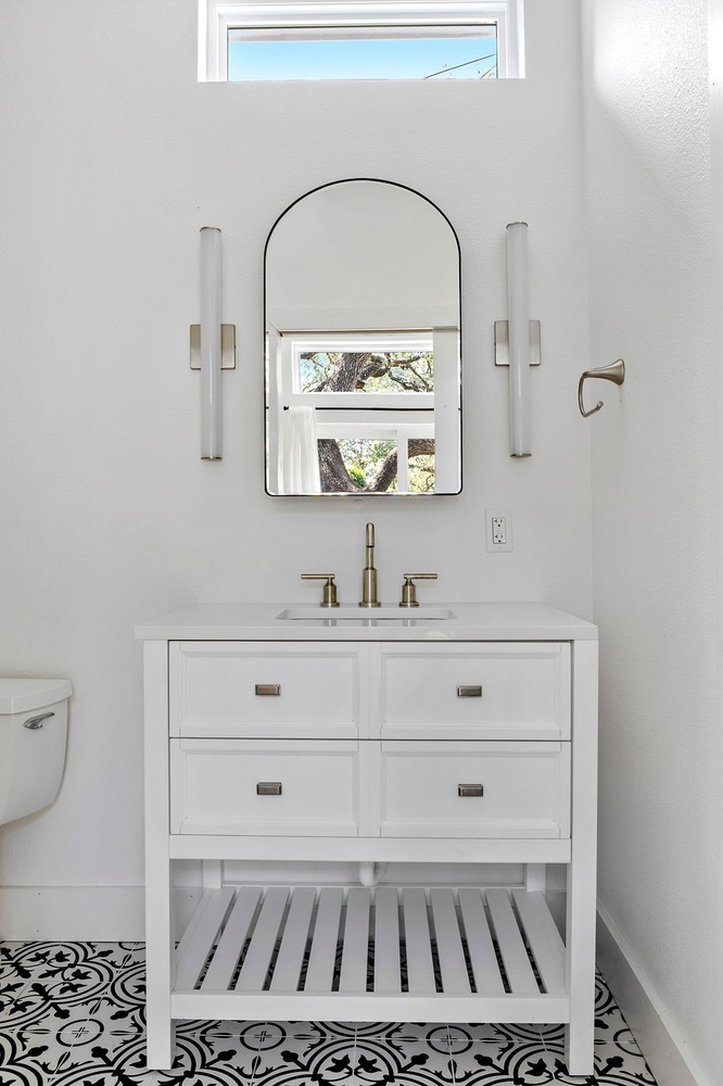 ADU bathroom vanity by RedOven Builds in 3102 S Oak Dr TX with white cabinetry, brass fixtures, and arched mirror