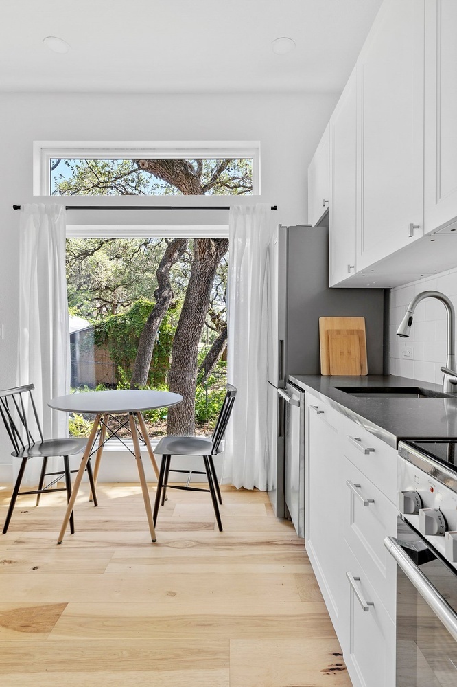 ADU kitchen dining corner by RedOven Builds in 3102 S Oak Dr TX with white cabinetry and large window view