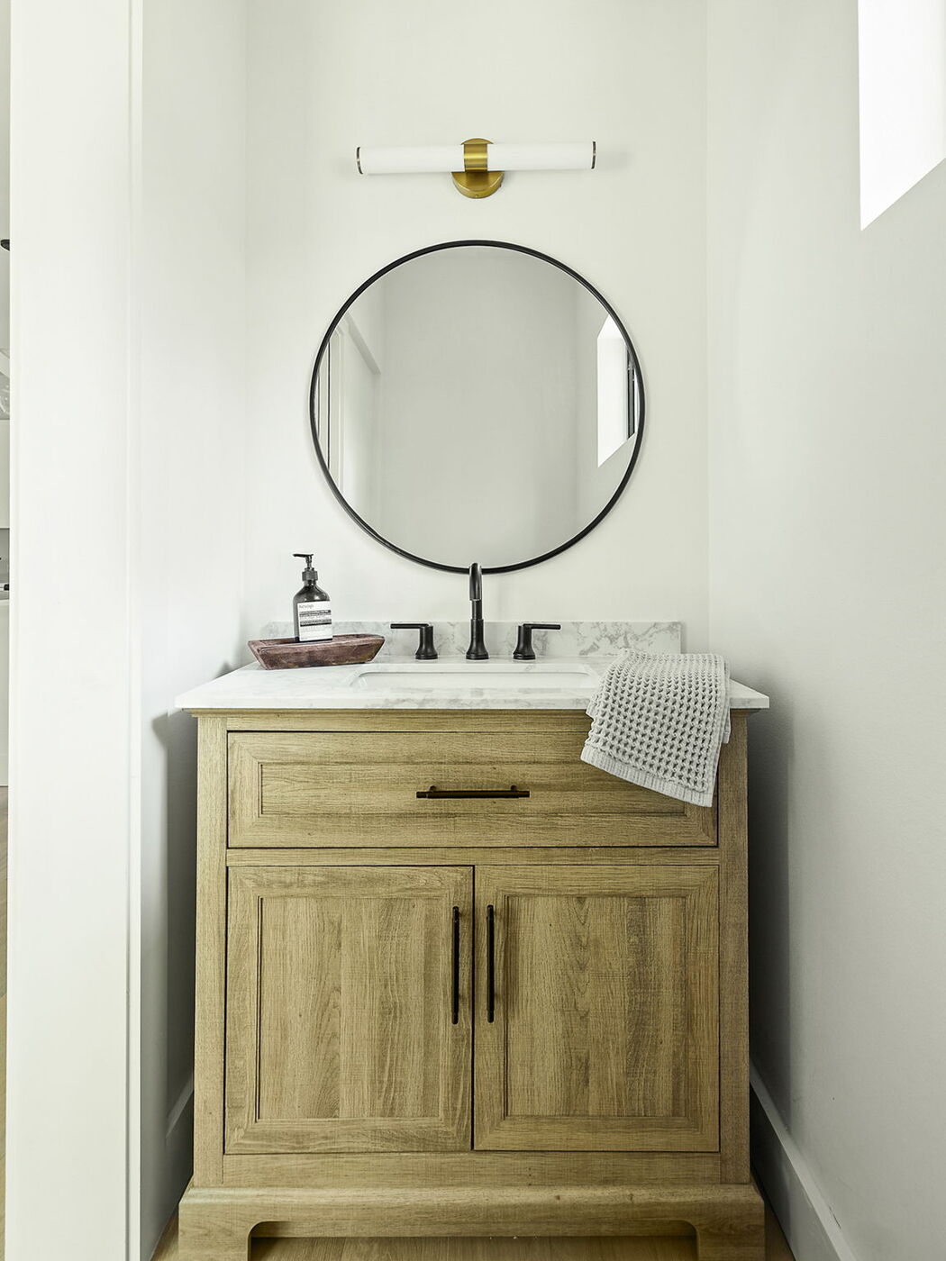 Bathroom vanity with wood cabinetry, marble countertop, and round mirror in Brentwood, TX ADU by RedOven Builds
