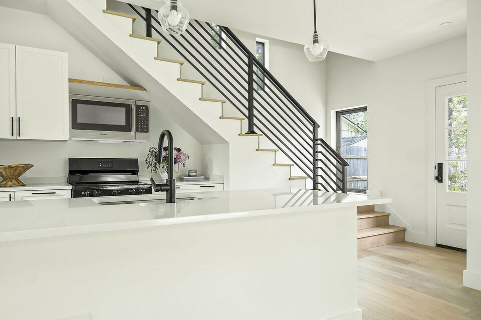 Bright kitchen with white cabinetry, island, and staircase near entry door in Brentwood, TX ADU by RedOven Builds