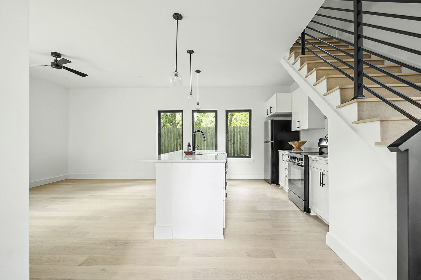Bright kitchen with white island, black railing staircase, and wood floors in Brentwood, TX ADU by RedOven Builds