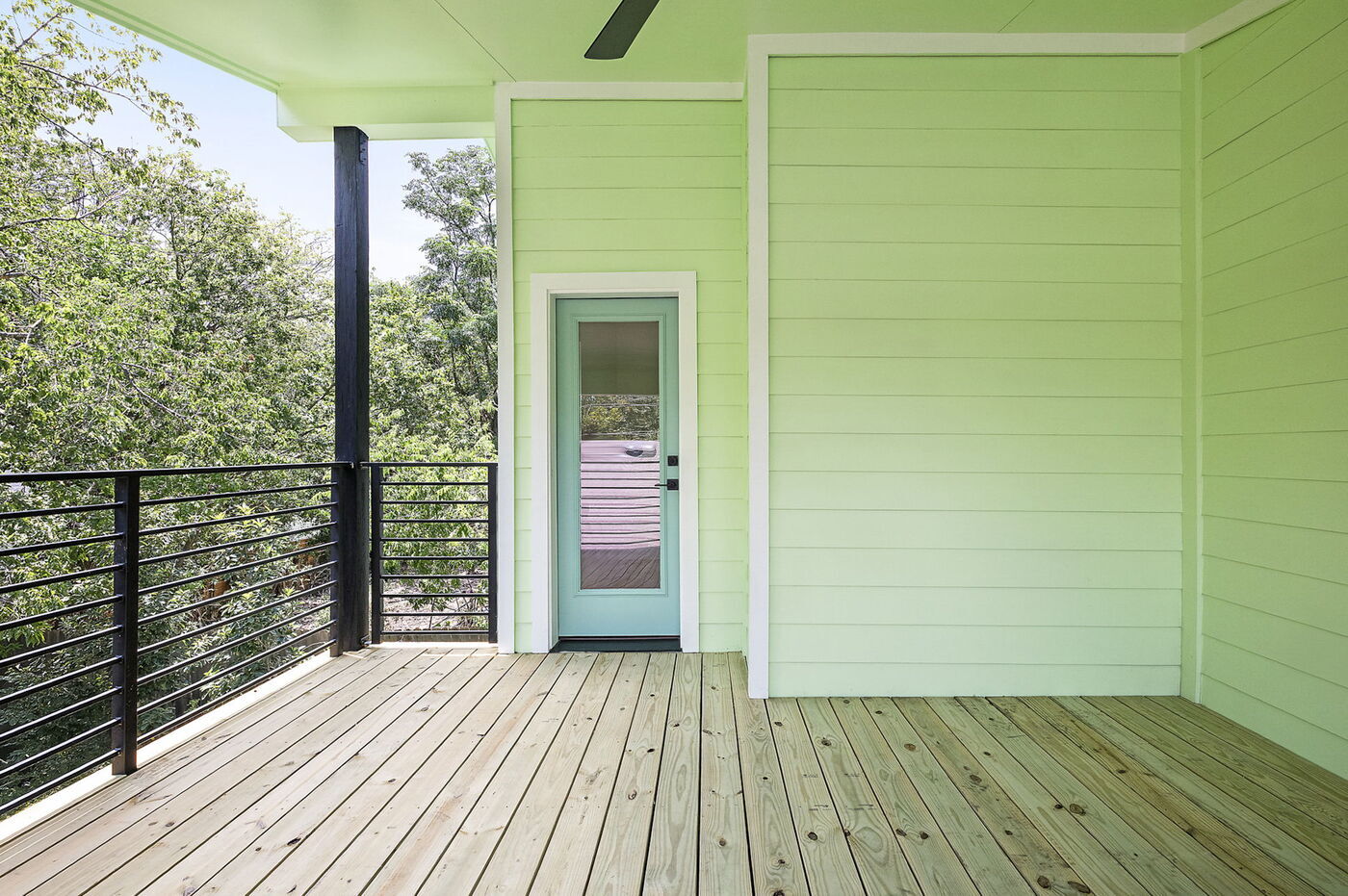 Covered balcony with wood decking, green siding, and glass door in Brentwood, TX ADU by RedOven Builds