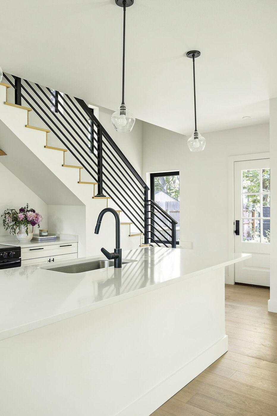 Kitchen island with black faucet, pendant lights, and staircase view in Brentwood, TX ADU by RedOven Builds