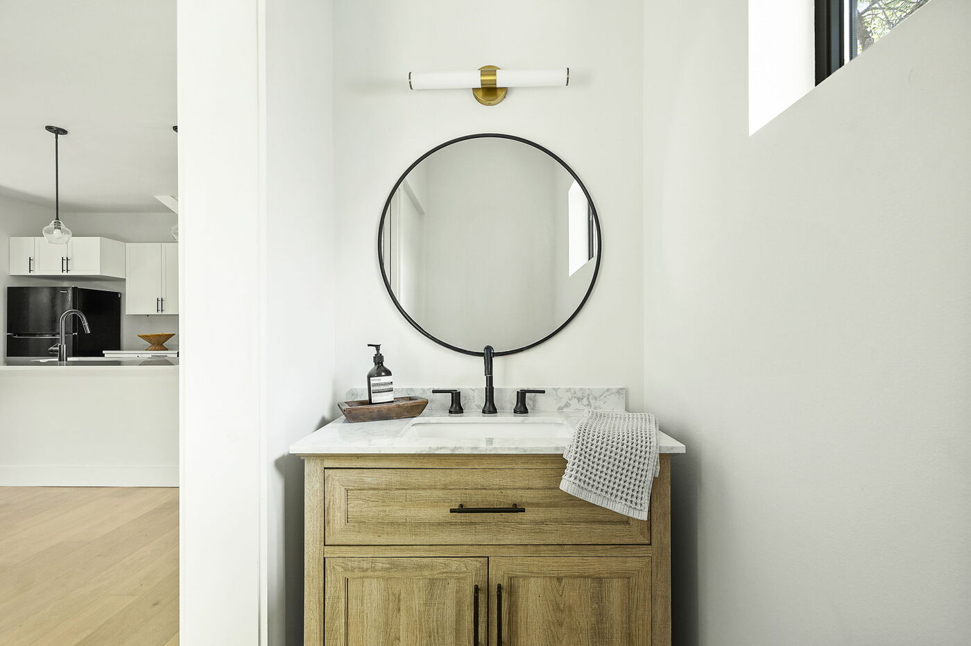 Modern bathroom vanity with round mirror, marble top, and wood cabinet in Brentwood, TX ADU by RedOven Builds
