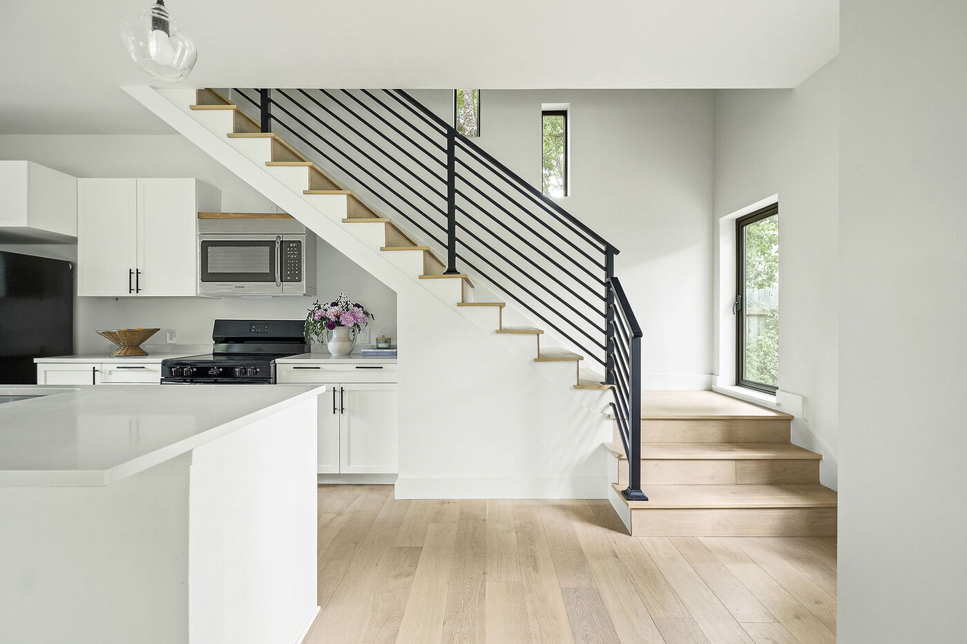 Modern kitchen with white island and black railing staircase in Brentwood, TX ADU by RedOven Builds