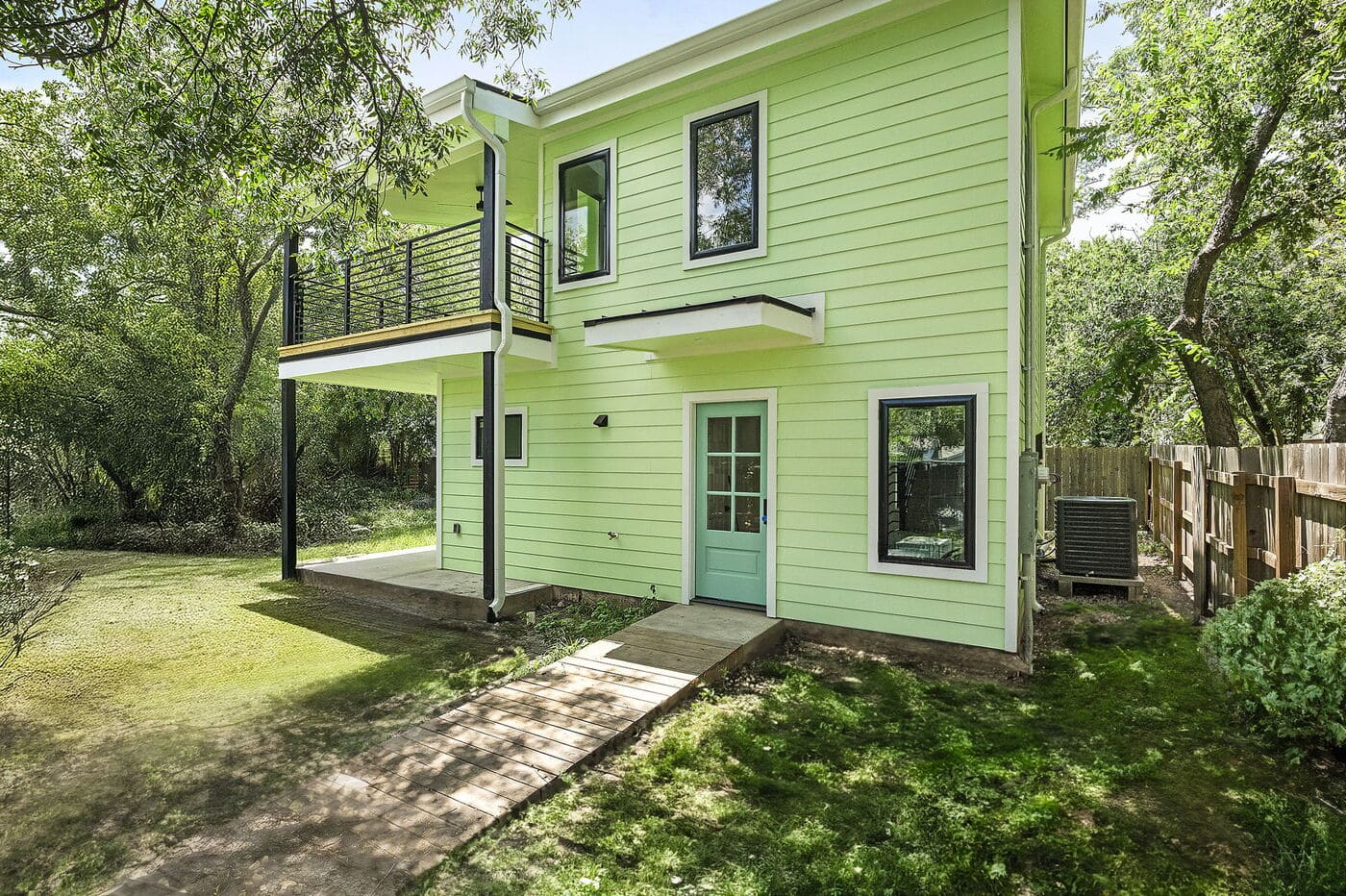 Rear view of green ADU with balcony, yard, and entry door in Brentwood, TX by RedOven Builds