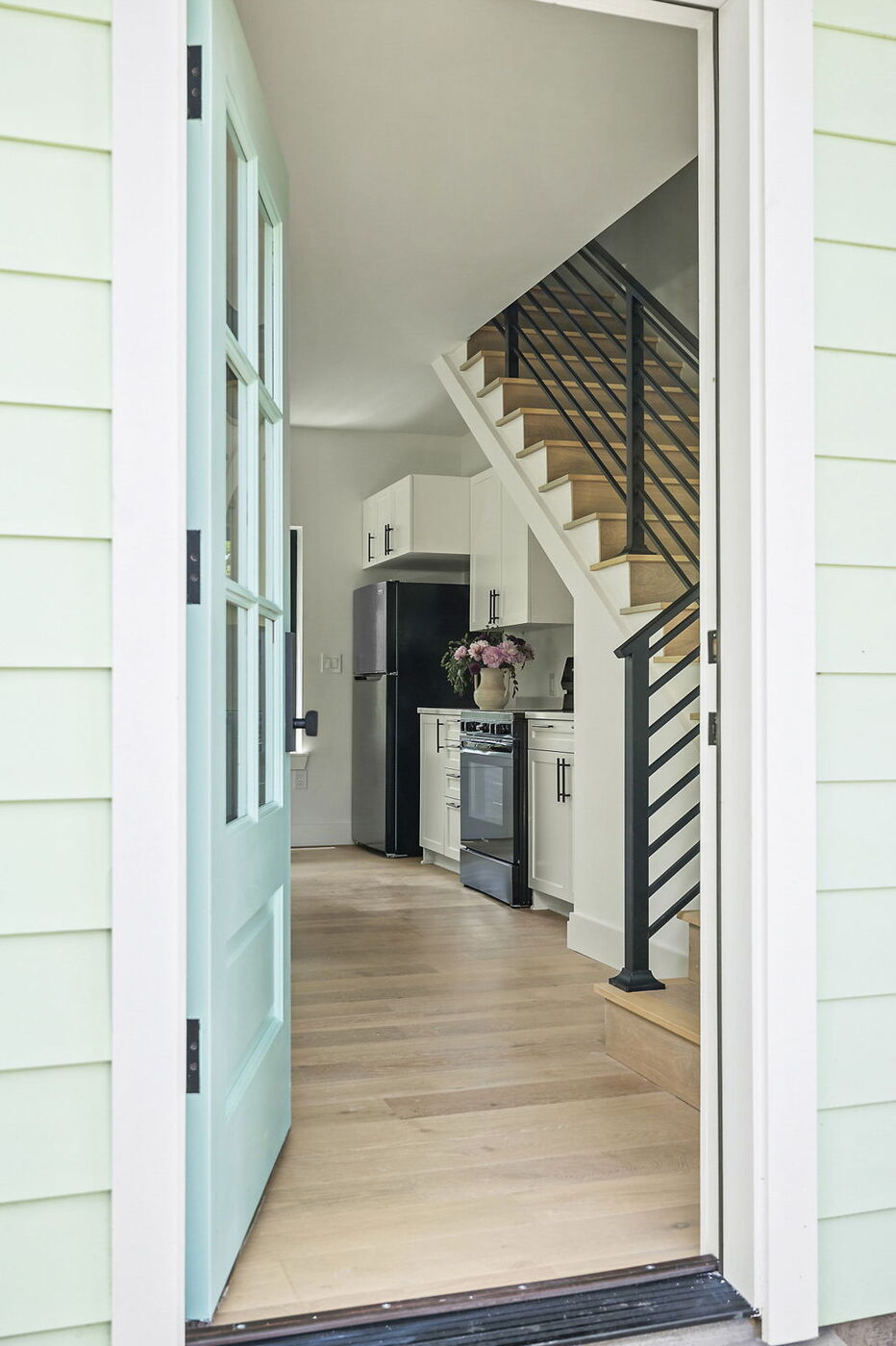 View into ADU kitchen with stairs, white cabinets, and wood floors in Brentwood, TX by RedOven Builds