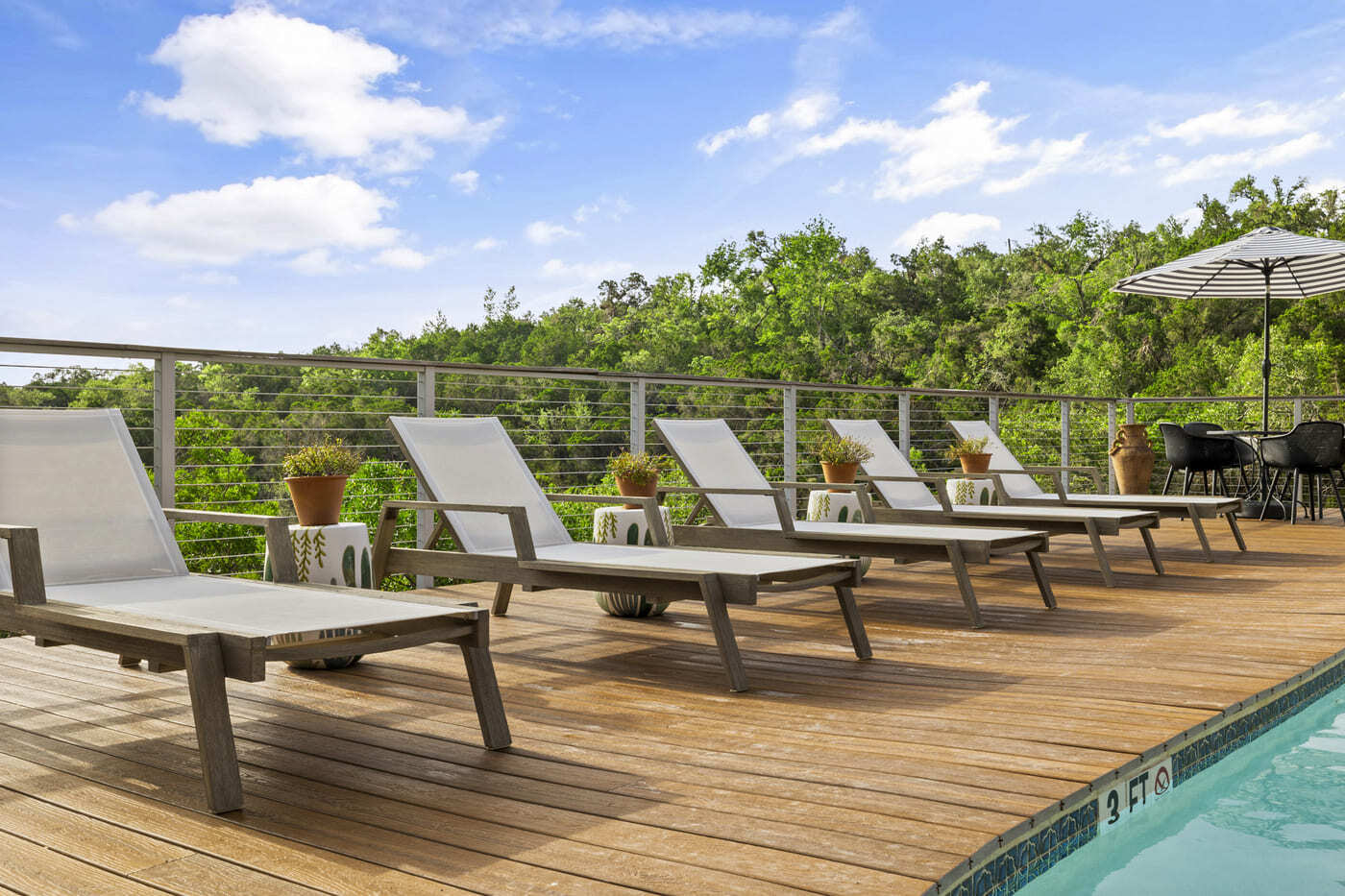 Hotel renovation poolside lounge chairs on wood deck in Austin, TX by RedOven Builds with hill country views