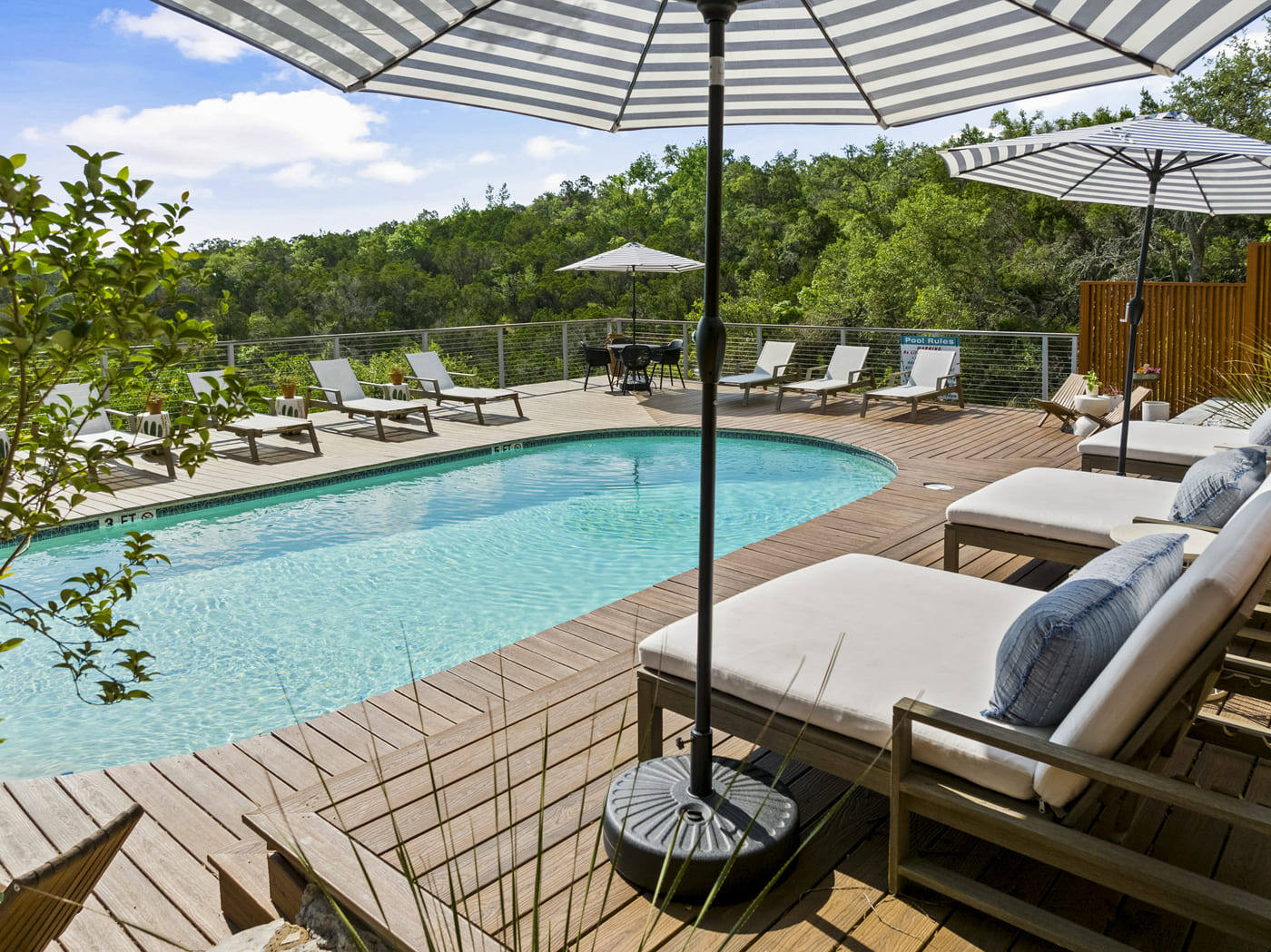 Pool deck and seating at a renovated hotel in Austin, TX by RedOven Builds with umbrellas, loungers, and wooded surroundings