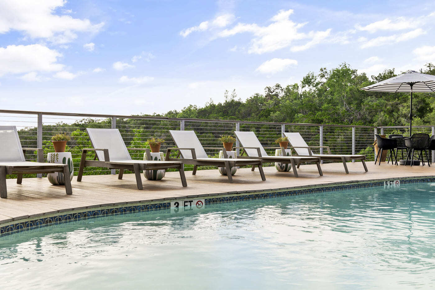 Pool edge with loungers and railing at a hotel renovation in Austin, TX by RedOven Builds overlooking wooded landscape