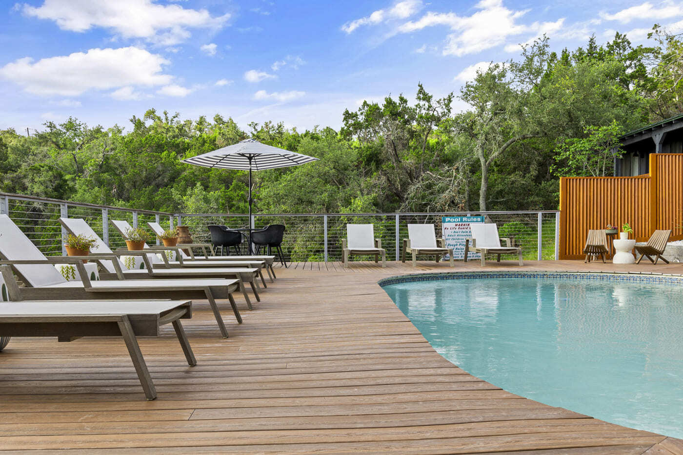 Spacious pool deck at hotel renovation in Austin, TX by RedOven Builds with seating, umbrellas, and wooded backdrop