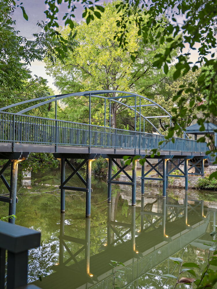 RedOven Builds commercial remodel steel pedestrian bridge over water at 4408 Long Champ Dr Austin TX surrounded by trees
