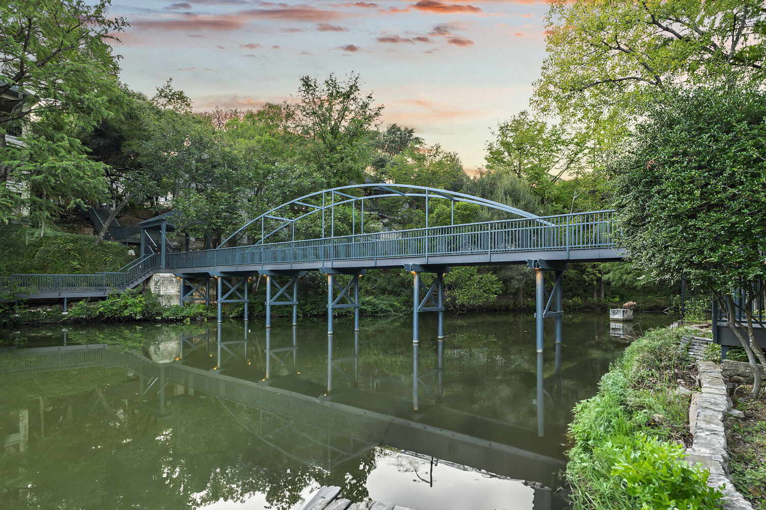 RedOven Builds commercial remodel steel pedestrian bridge spanning water at 4408 Long Champ Dr Austin, TX surrounded by trees