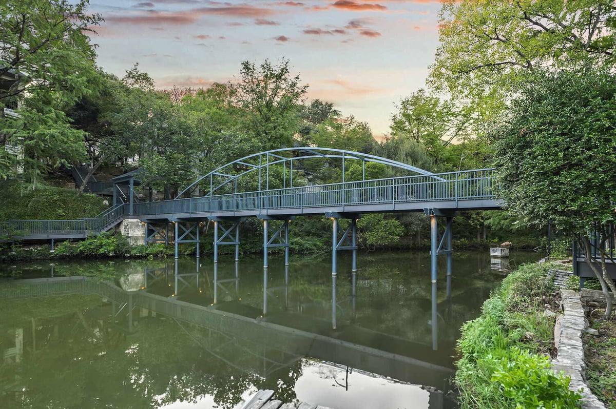 RedOven Builds commercial remodel steel pedestrian bridge spanning water at 4408 Long Champ Dr Austin, TX surrounded by trees