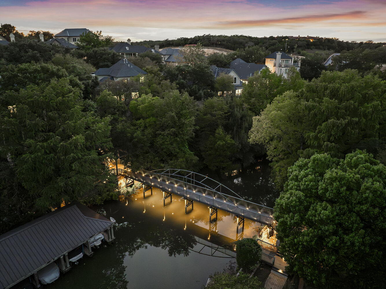 dusk aerial of custom lit bridge spanning creek by RedOven Builds in Austin TX