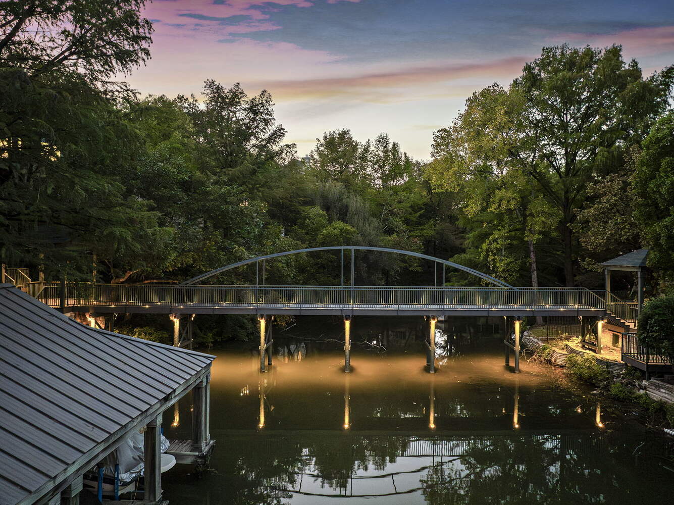 evening view of illuminated pedestrian bridge spanning creek by RedOven Builds in Austin TX