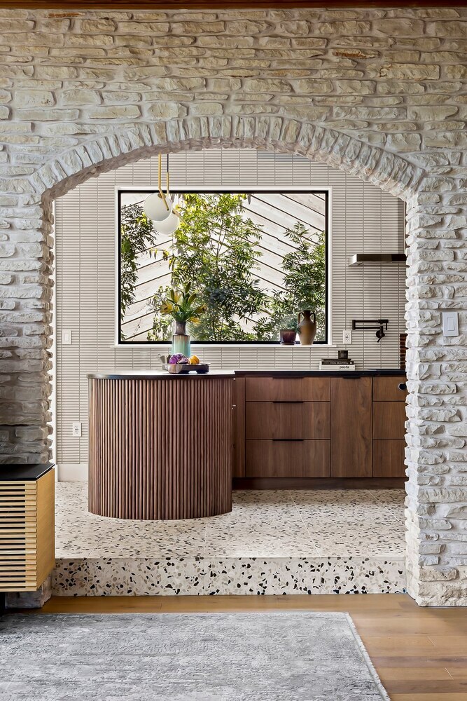 Custom kitchen design by RedOven Builds in Austin TX with textured stone archway and modern wood island