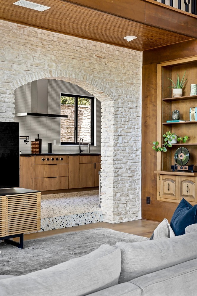 Modern living room and kitchen connection in Austin TX remodel by RedOven Builds with stone arch and wood finishes