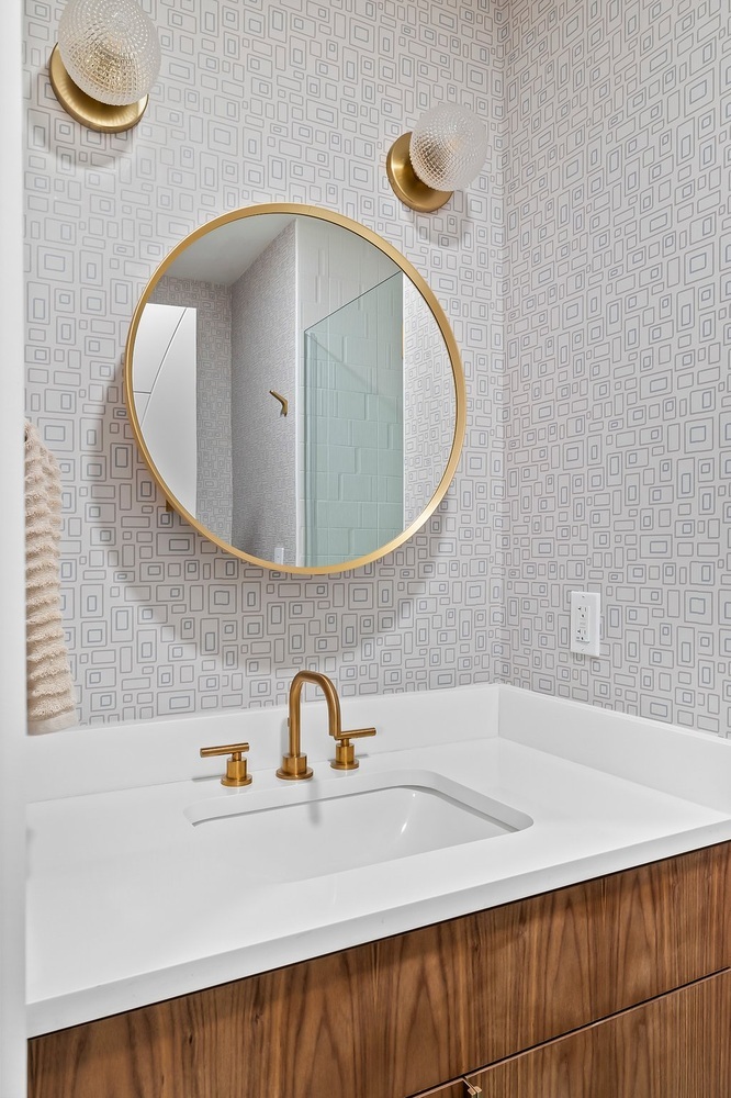 close up of modern bathroom sink with brass faucet and round mirror by RedOven Builds in Austin TX remodel