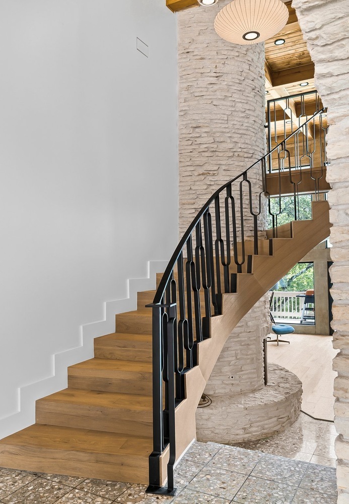 curved staircase with black metal railing and stone walls in Austin TX by RedOven Builds