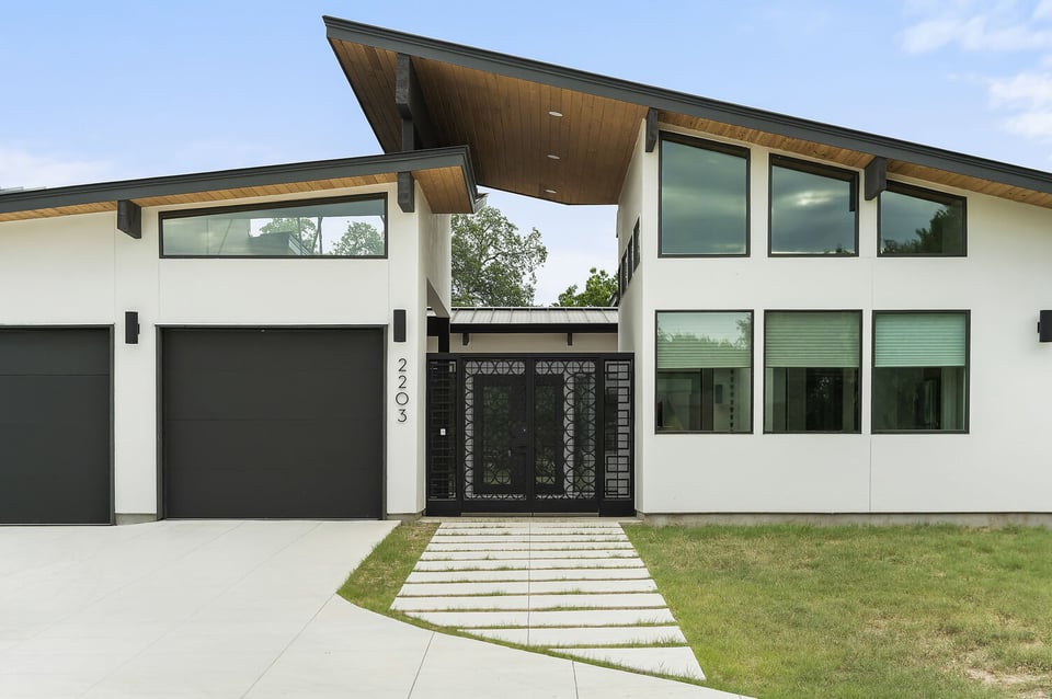 RedOven Builds custom home exterior in Austin TX with modern facade, black garage doors, and geometric entry gate